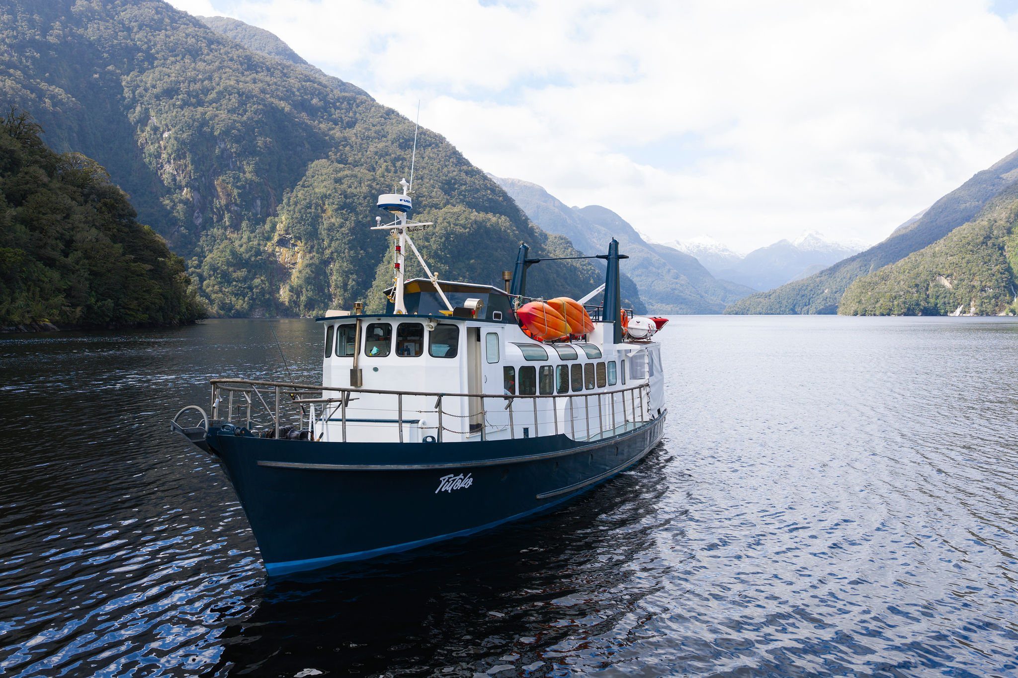 MV Tutoko, Fiordland Expeditions' 16 metre expedition vessel, in Doubtful Sound with snow-capped peaks behind