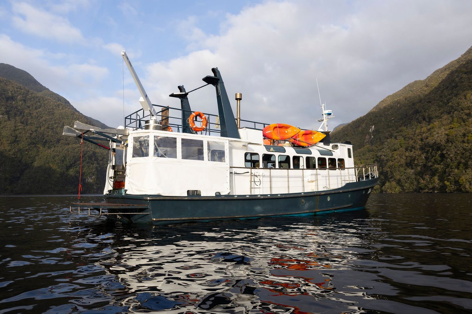 MV Tutoko at anchor in Fiordland with orange kayaks stowed on the upper deck